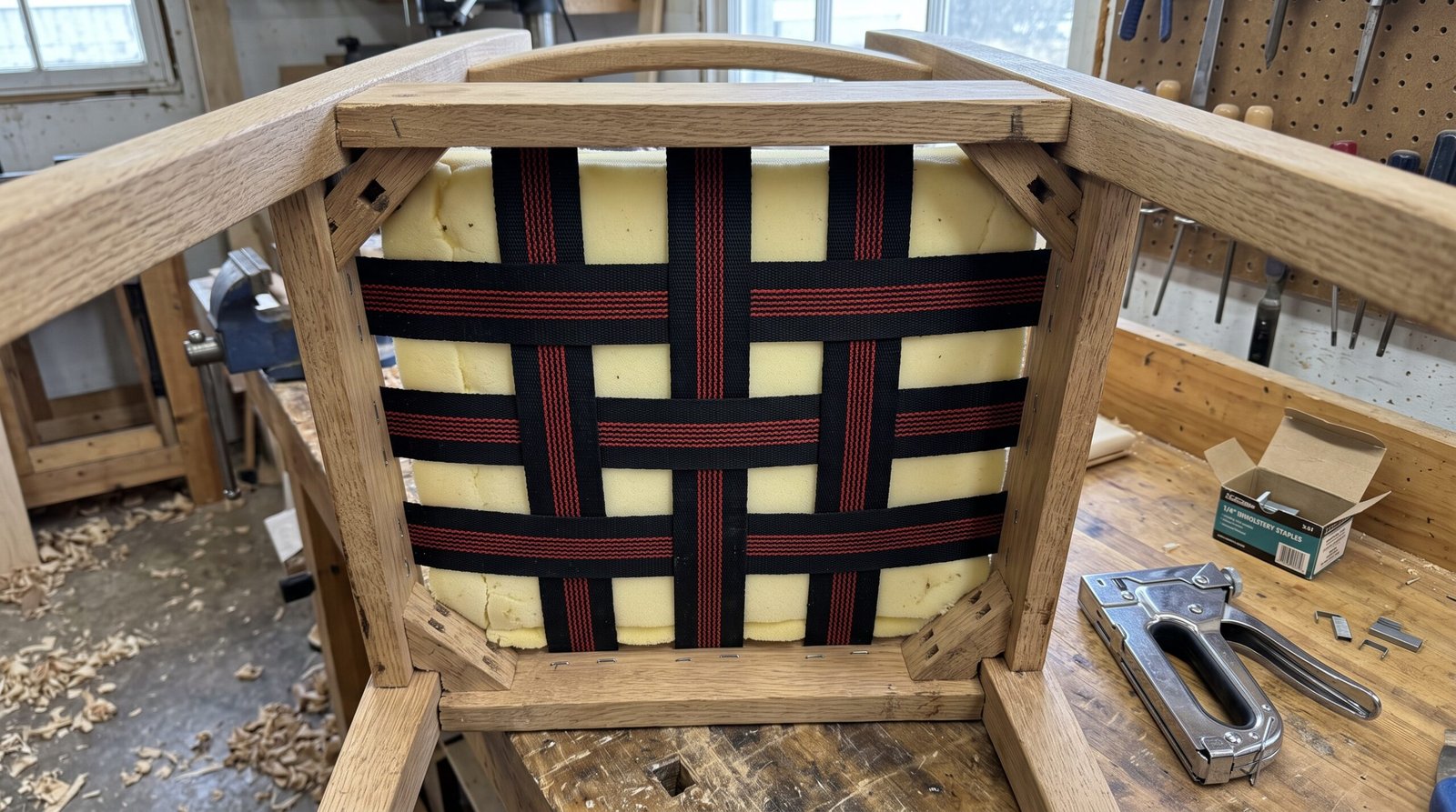 Underside view of a dining chair showing webbing straps, foam, and wooden frame